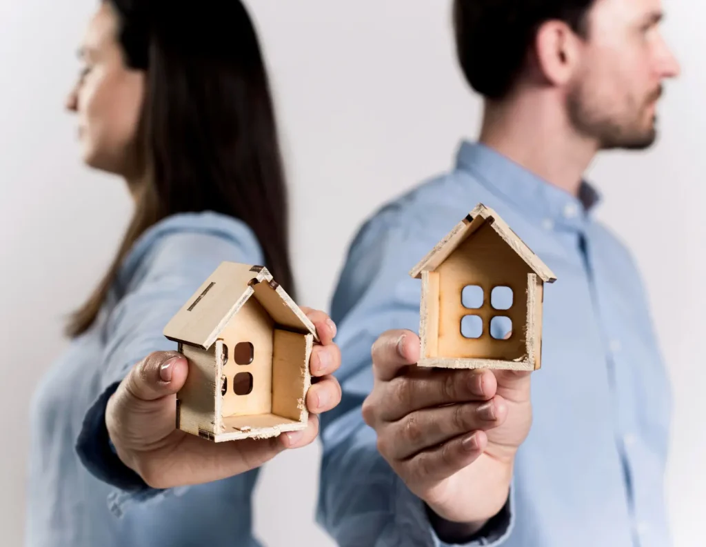 Pareja de espaldas sosteniendo casas en miniatura como símbolo de la separación de bienes y reparto patrimonial.